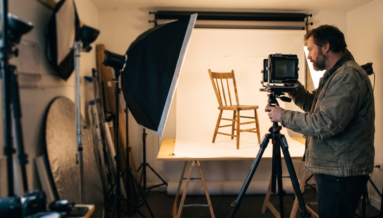 En fotograf som justerar en softbox över ett stylat möbelset i en dagsljusstudio
