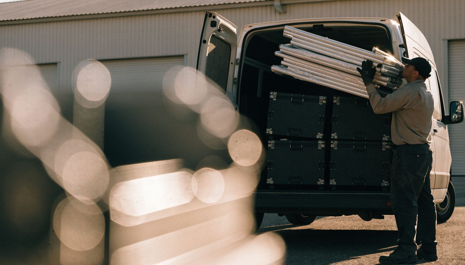 A worker loading folded marquee frames into the back of a van outside a rental depot
